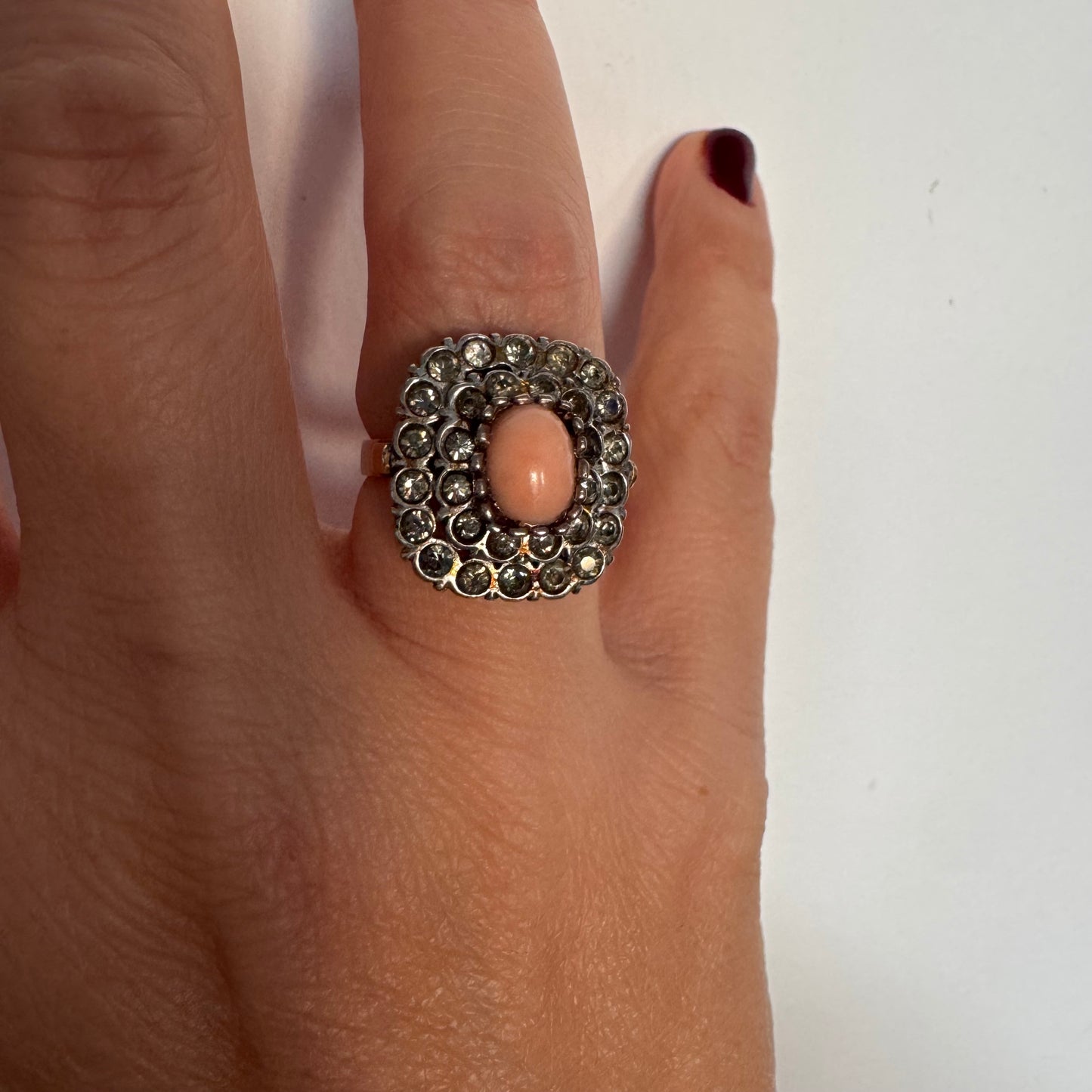 טבעת וינטג׳ עם חלק תחתון מזהב 14 קראט וחלק עליון עשוי כסף משובצת אבן קורל טבעית במרכז ומסביבה אבנים בהירות שאינן יהלומים.