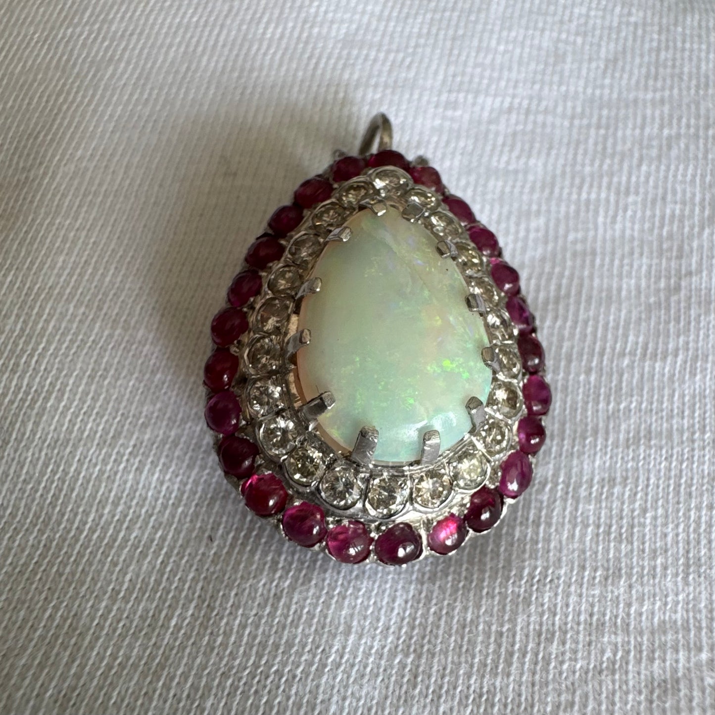 תליון זהב 14 קראט משובץ אבן אופל בחיתוך טיפה, מוקפת בשתי מסגרות של יהלומים ורובי נוצצים. 