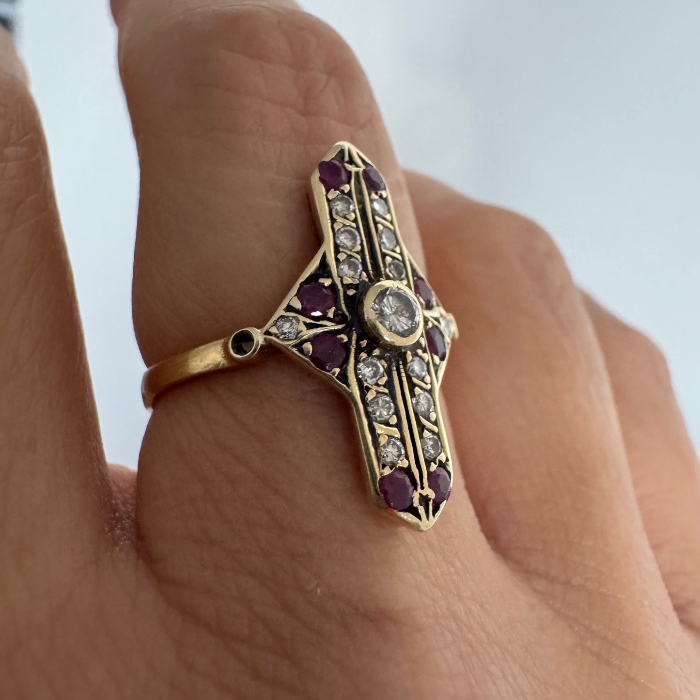 18K gold ring featuring a striking geometric design, set with a central Diamond surrounded by sparkling Diamonds and rich red Rubies.