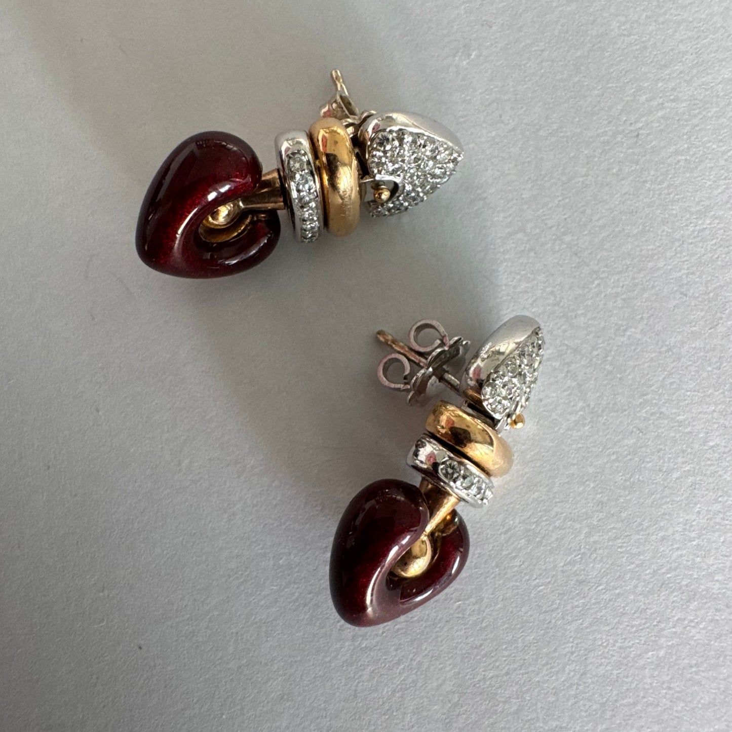עגילי זהב 18 קראט בשילוב זהב צהוב ולבן, משובצים יהלומים בחלק העליון ובחישוק מרכזי, ובתחתית תליון לב אדום בגימור מבריק.