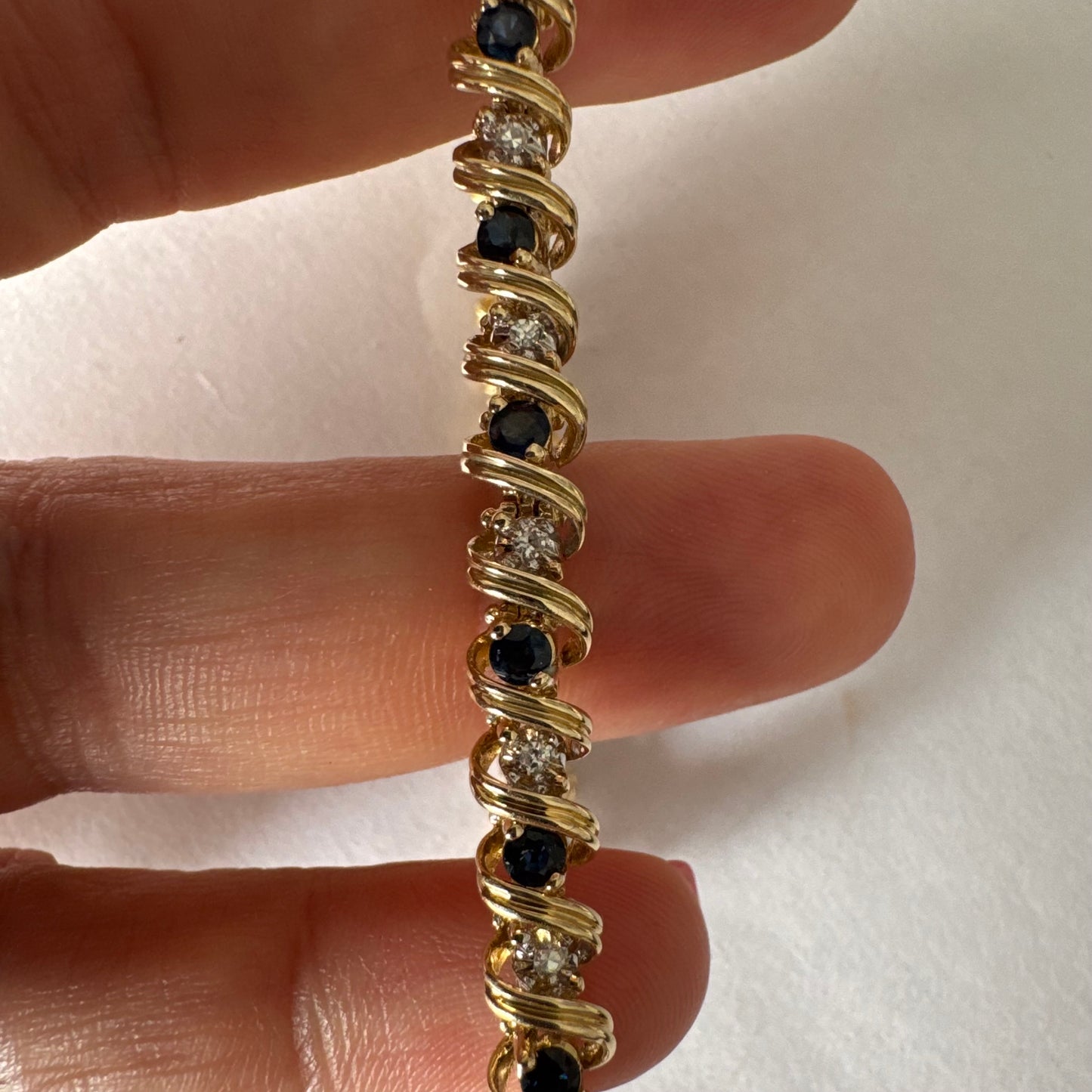 צמיד זהב צהוב 14 קראט משובץ אבני ספיר כחולות ויהלומים, המשובצים בעיצוב זורם עם קווים מעוגלים העוטפים כל אבן.