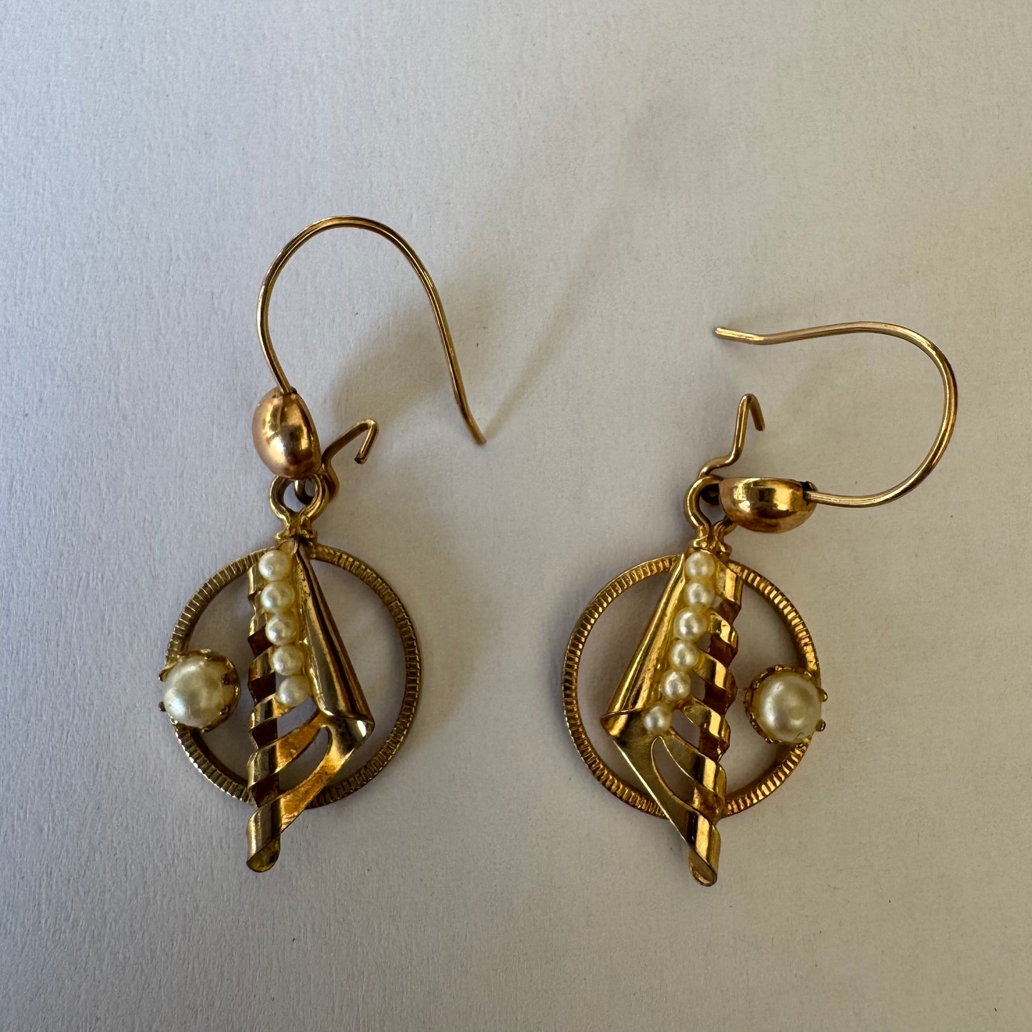 עגילי זהב 10 קראט, בעיצוב עדין עם אלמנט ספירלי ושילוב פנינים קטנות בגוון לבן-קרם. 