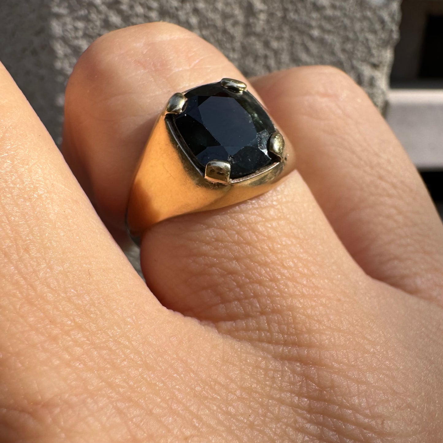 טבעת זהב 9 קראט משובצת ספיר ירוק כהה בחיתוך כרית ובתפסים עבים, בעיצוב נקי ובעל נוכחות. 