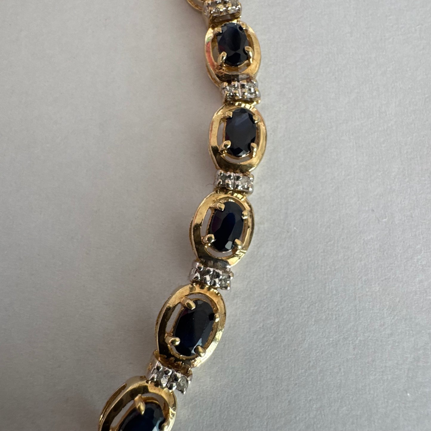 צמיד זהב צהוב 10 קראט בעיצוב קלאסי ועשיר, משובץ אבני ספיר אובליות בגוון כחול עמוק וביניהן שיבוצי יהלומים לבנים עדינים.