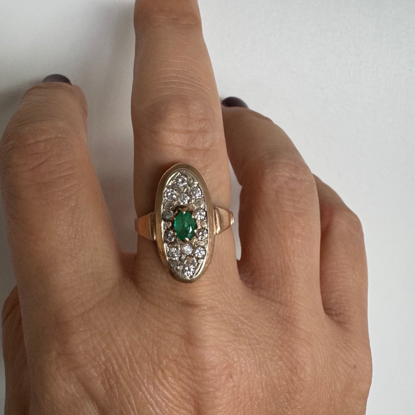 טבעת זהב 14 קראט בעיצוב אלגנטי ומאורך, משובצת אבן אמרלד מרכזית ויהלומים מסביב.
