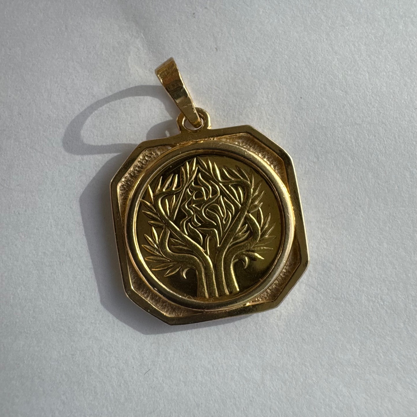 תליון זהב צהוב 14 קראט בעיצוב קלאסי עם נוכחות סמלית חזקה. במרכז התליון חריטה עדינה של עץ חיים, סמל לצמיחה, חיבור ושפע וכיתוב ״שמע ישראל״ ובצד השני אותיות ה-א״ב.