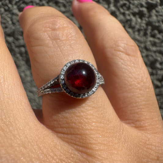 14K gold ring set with a deep red cabochon Garnet, surrounded by a halo of sparkling Diamonds