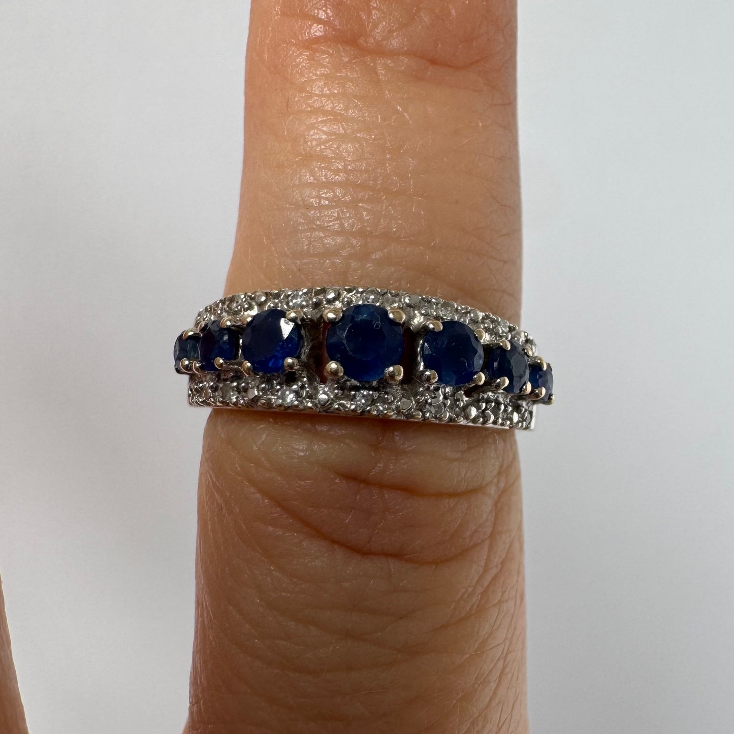 18K gold ring set with deep blue sapphires in a classic round cut, framed by two shimmering rows of brilliant Diamonds.