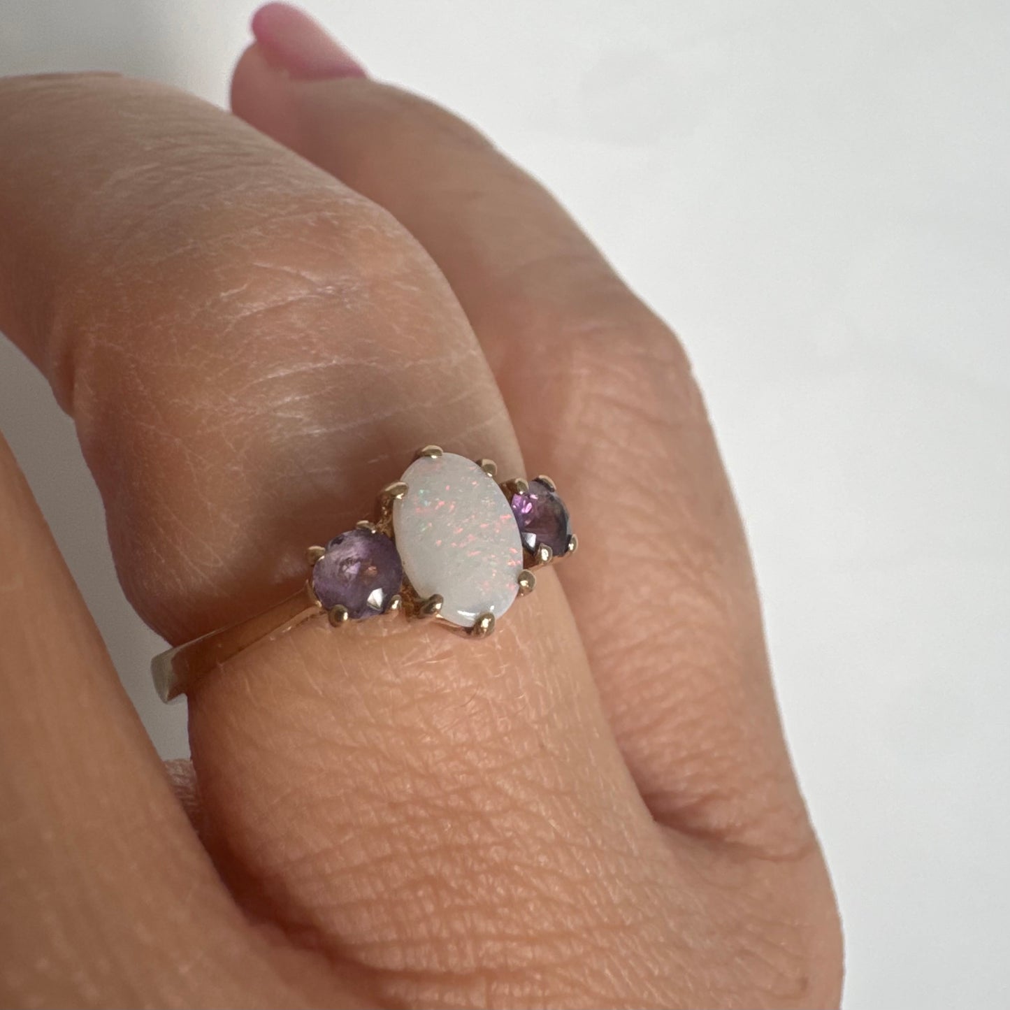 9K gold ring set with an oval Opal at the center, flanked by two delicate purple stones.