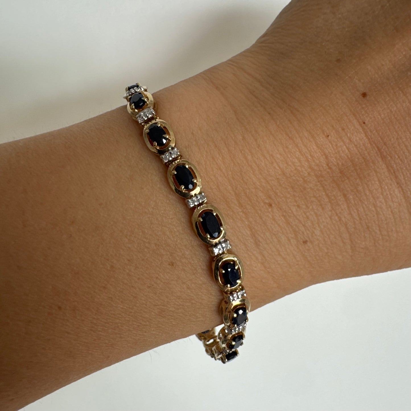 צמיד זהב צהוב 10 קראט בעיצוב קלאסי ועשיר, משובץ אבני ספיר אובליות בגוון כחול עמוק וביניהן שיבוצי יהלומים לבנים עדינים.