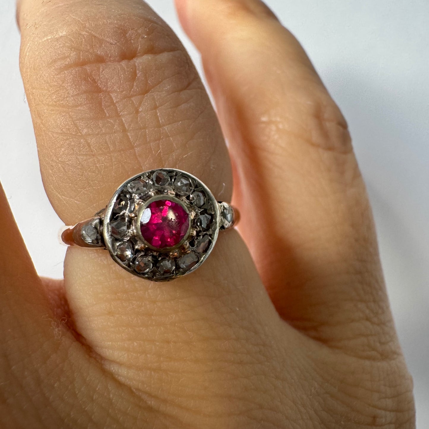 18K gold ring set with a round Ruby at the center, surrounded by a halo of old-cut Diamonds.