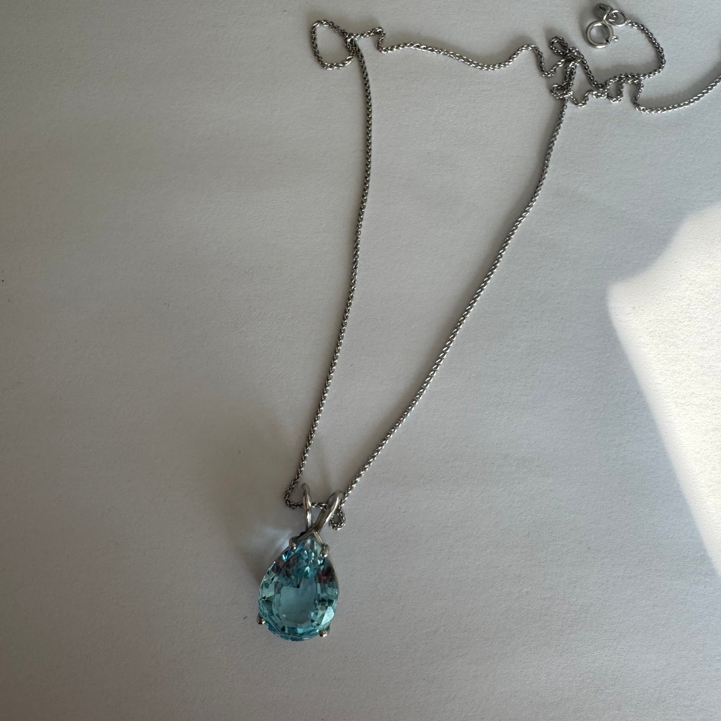 תליון זהב לבן 14 קראט המשובץ אבן טופז כחולה בחיתוך טיפה.