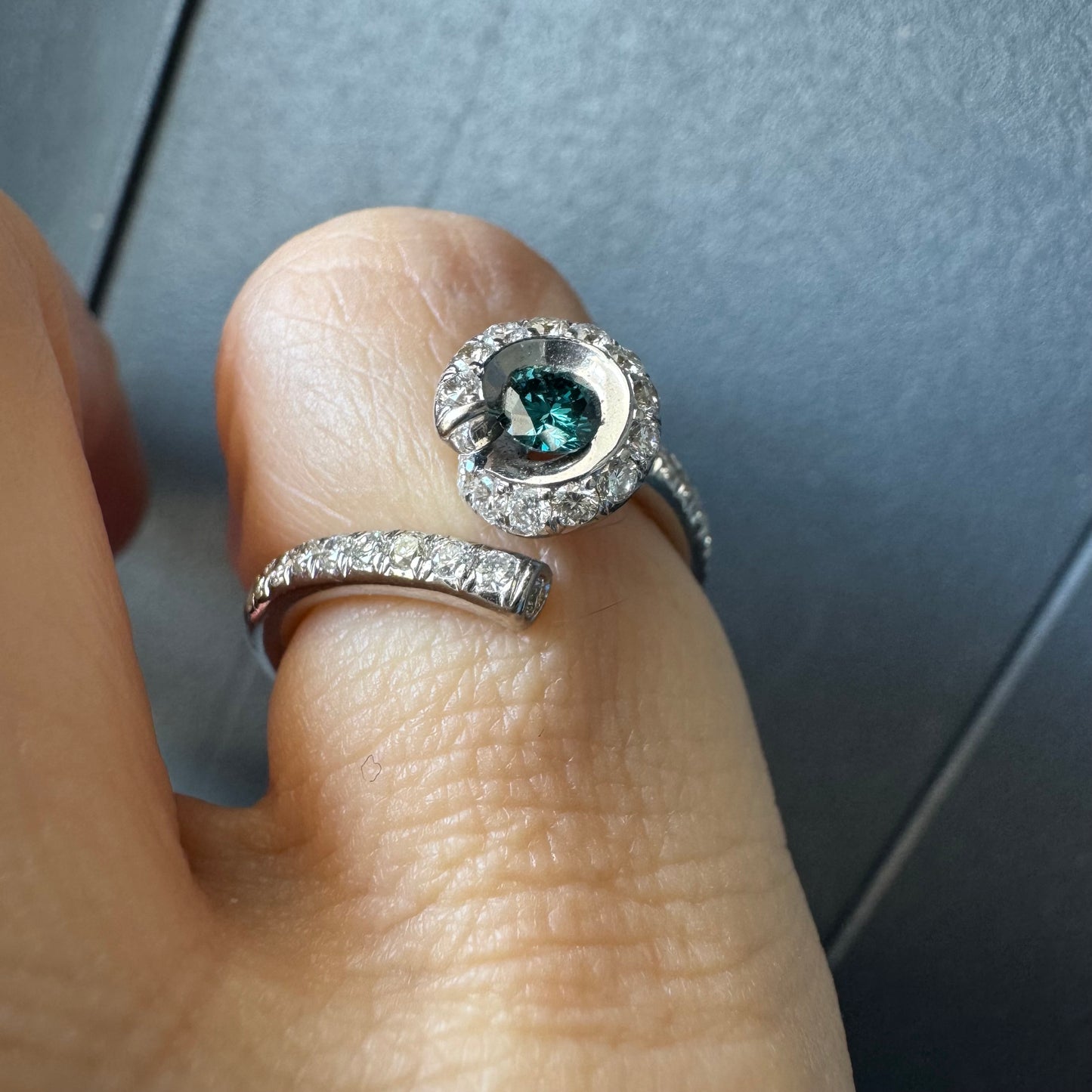 טבעת זהב לבן 18 במרכזה משובץ יהלום כחול עז, מוקף בהילה של יהלומים לבנים והזרועות של הטבעת משובצות יהלומים