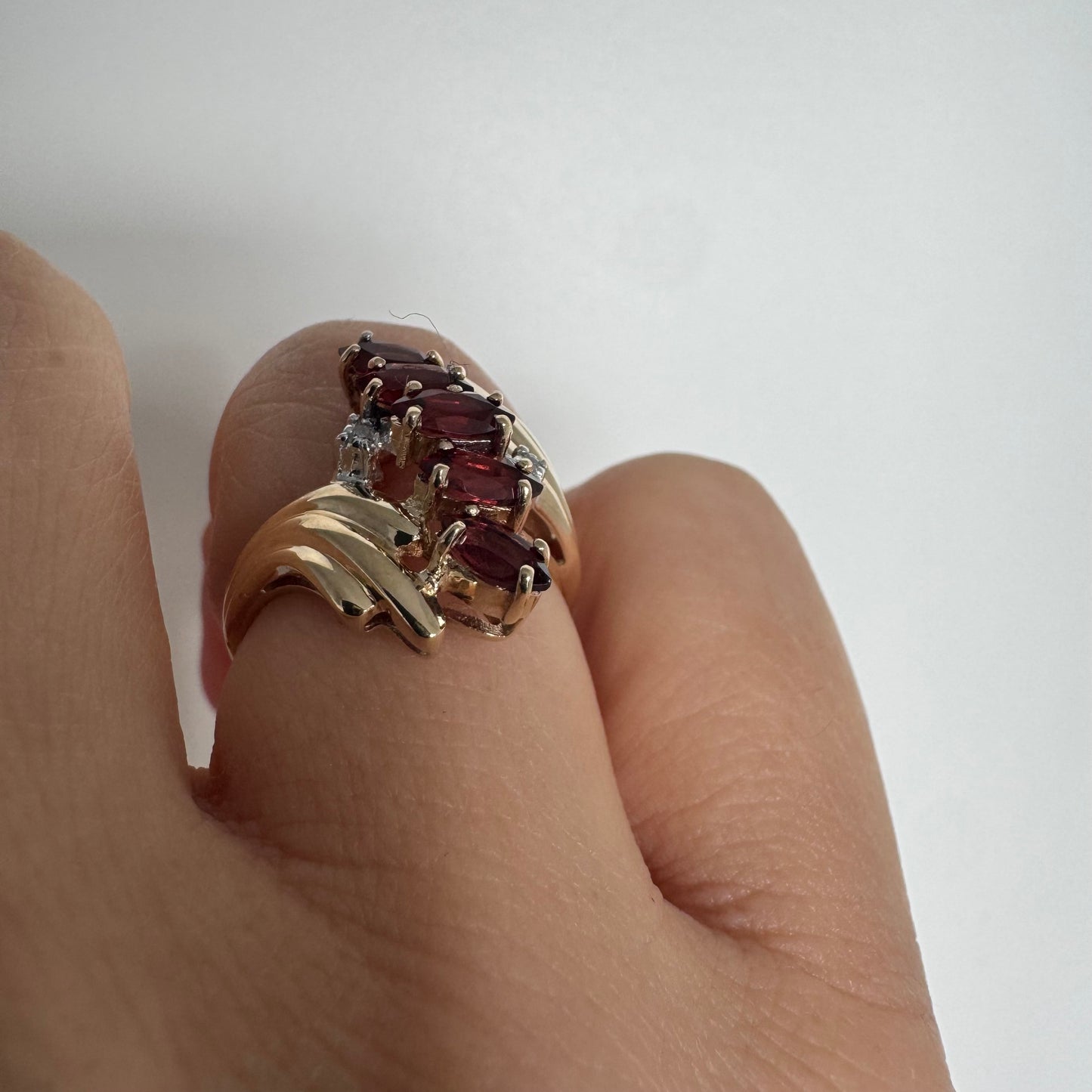 טבעת זהב צהוב 10 קראט בעיצוב דינמי ומלא תנועה, משובצת אבני גרנט בחיתוך מרקיזה בגוון אדום עמוק ובמרכזה נגיעות יהלומים לבנים.