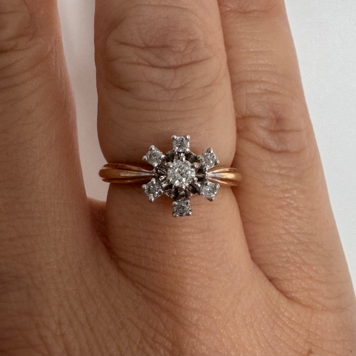 טבעת זהב 9 קראט משובצת יהלום מרכזי ויהלומים מסביב בעיצוב פרח קלאסי.