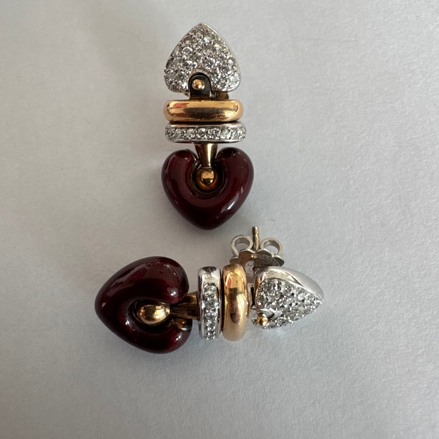 עגילי זהב 18 קראט בשילוב זהב צהוב ולבן, משובצים יהלומים בחלק העליון ובחישוק מרכזי, ובתחתית תליון לב אדום בגימור מבריק.