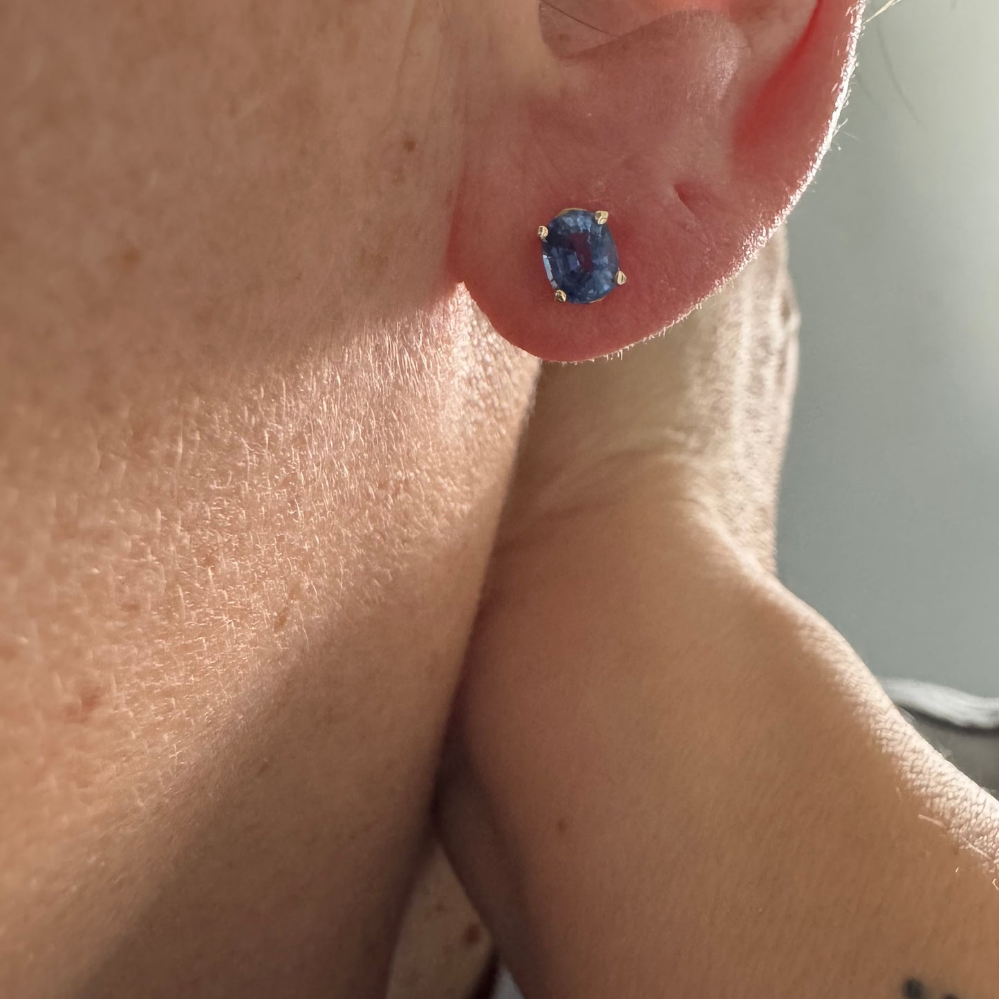 עגילי זהב 14 קראט קטנים צמודים לאוזן משובצים אבני טנזנייט בחיתוך אובלי, בגוון כחול־סגלגל עמוק ומעודן.