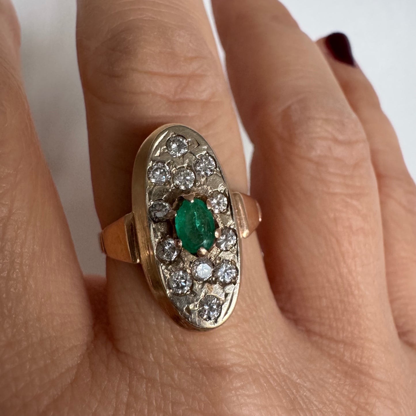 טבעת זהב 14 קראט בעיצוב אלגנטי ומאורך, משובצת אבן אמרלד מרכזית ויהלומים מסביב.