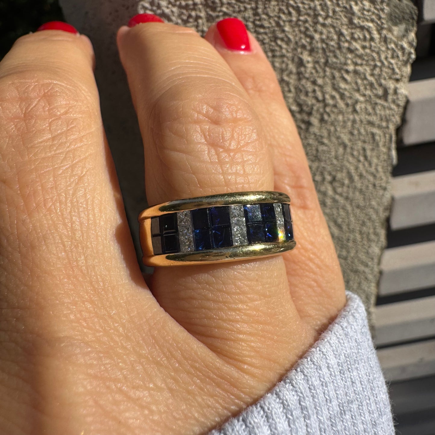 טבעת ה.שטרן זהב צהוב 18 קראט, בעיצוב רחב ומרשים. משובצת שורת אבני ספיר כחולות מרובעות בשילוב מחיצות של יהלומים לנגיעת ברק יוקרתי.