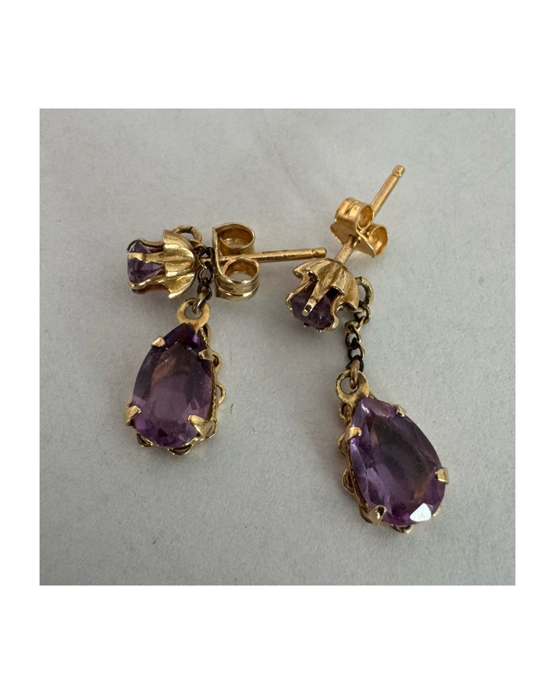 עגילים זהב צהוב 14 קראט משובצים אבני אמטיסט בגוון סגול עמוק בחיתוך טיפה, בשילוב אבן עליונה תואמת ועיטור שרשרת עדינה המחברת ביניהן.