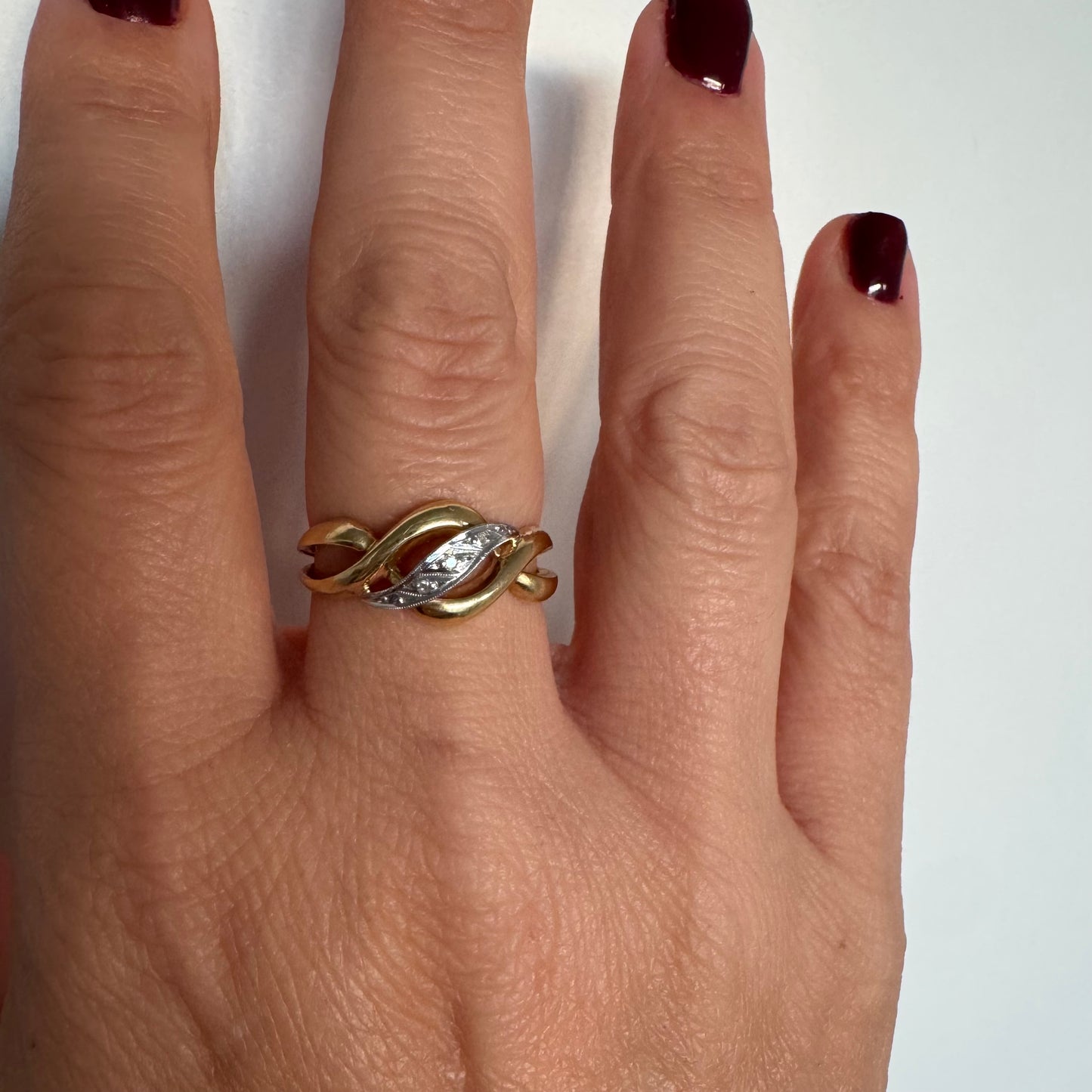 טבעת זהב צהוב 18 קראט בעיצוב קשר קלאסי, בשילוב אלמנט מרכזי מזהב לבן משובץ יהלומים עדינים.