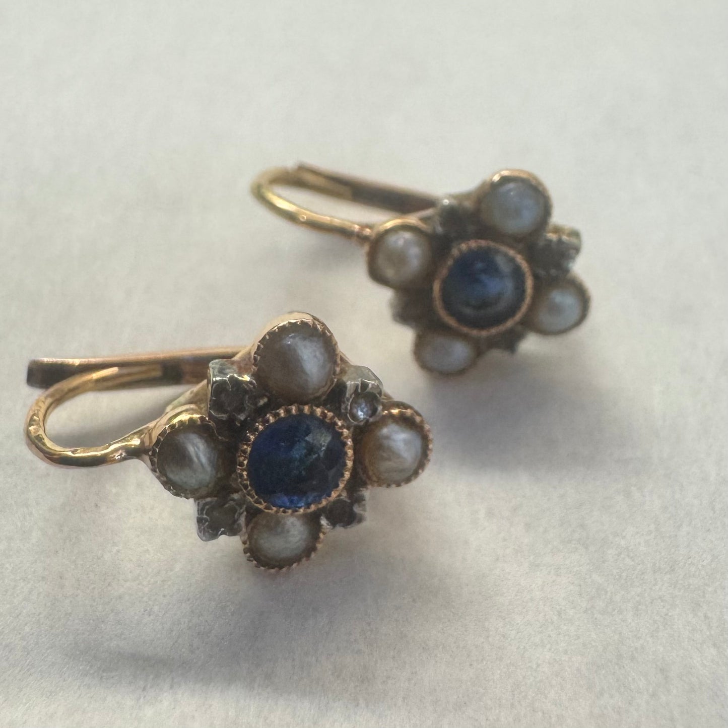 14K gold earrings featuring a round deep blue Sapphire in the center, surrounded by Pearls arranged in a floral design.