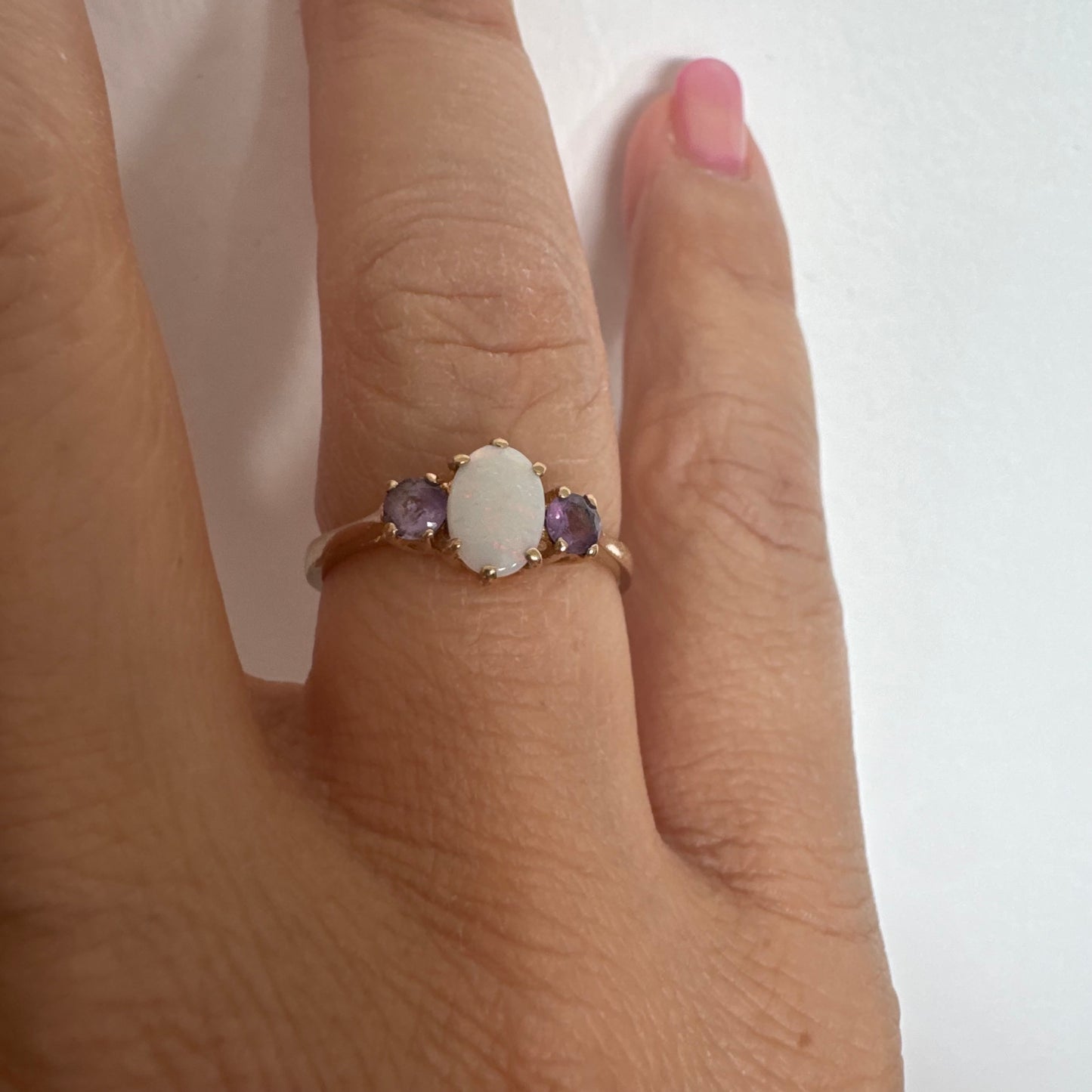 9K gold ring set with an oval Opal at the center, flanked by two delicate purple stones.
