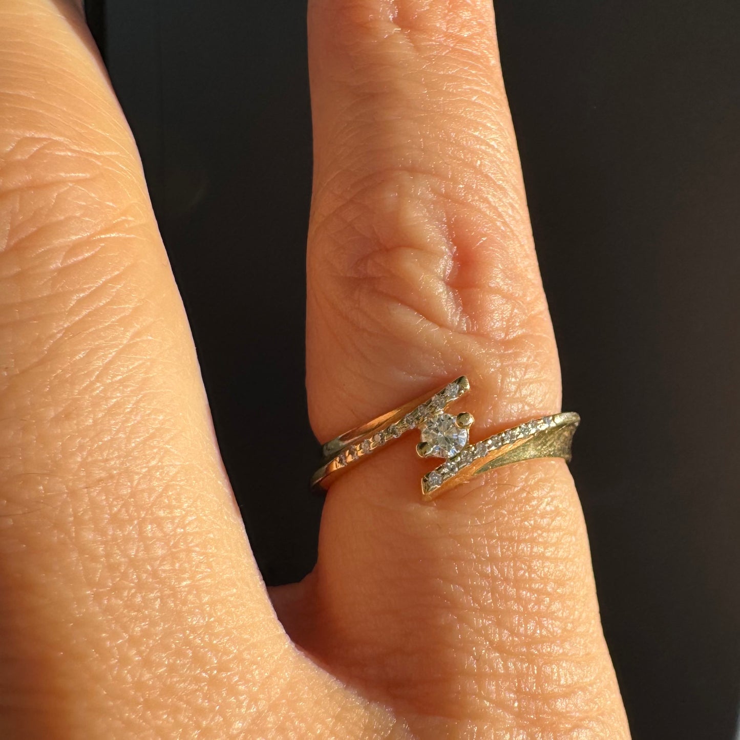 טבעת זהב 14 קראט בעיצוב פתוח ואלגנטי, משובצת יהלום מרכזי ויהלומים עדינים לאורך הזרועות.