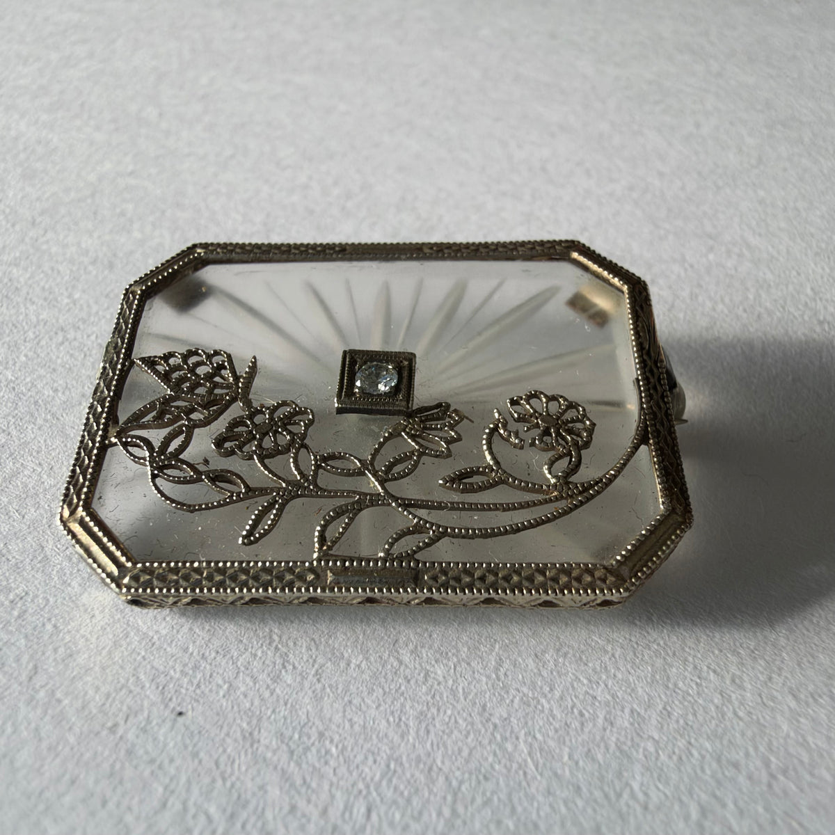 An antique Art-Deco brooch featuring a geometric design, delicate floral details & a sparkling Diamond