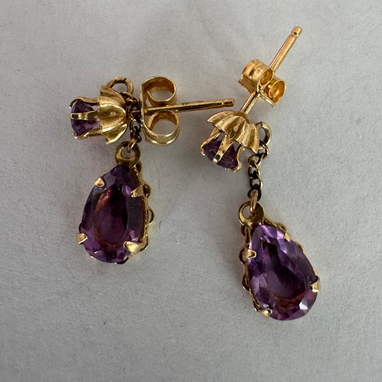 עגילים זהב צהוב 14 קראט משובצים אבני אמטיסט בגוון סגול עמוק בחיתוך טיפה, בשילוב אבן עליונה תואמת ועיטור שרשרת עדינה המחברת ביניהן.