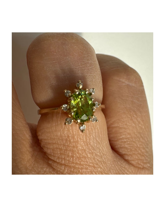 טבעת זהב 14 קראט משובצת אבן פרידוט ירוקה בחיתוך אובלי, מוקפת יהלומים היוצרים הילה עדינה מסביבה.