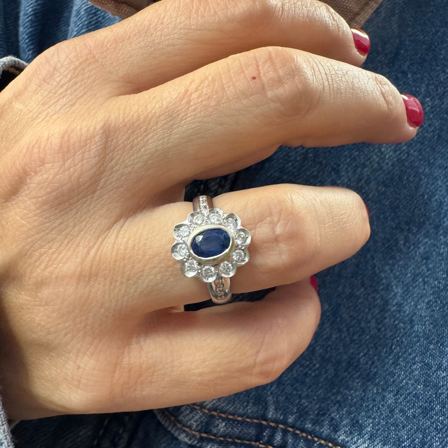 18K gold ring set with an oval blue Sapphire surrounded by a halo of round Diamonds in a flower-shaped design.