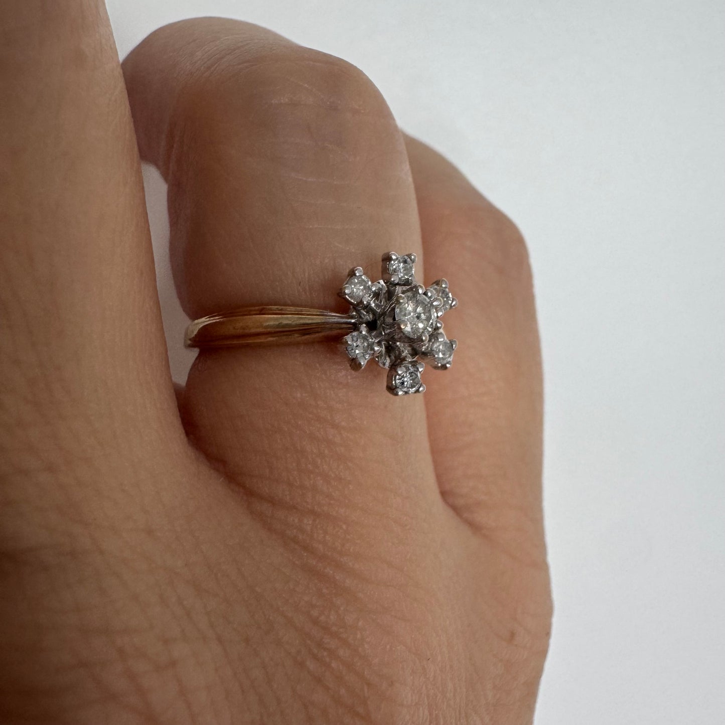 טבעת זהב 9 קראט משובצת יהלום מרכזי ויהלומים מסביב בעיצוב פרח קלאסי.