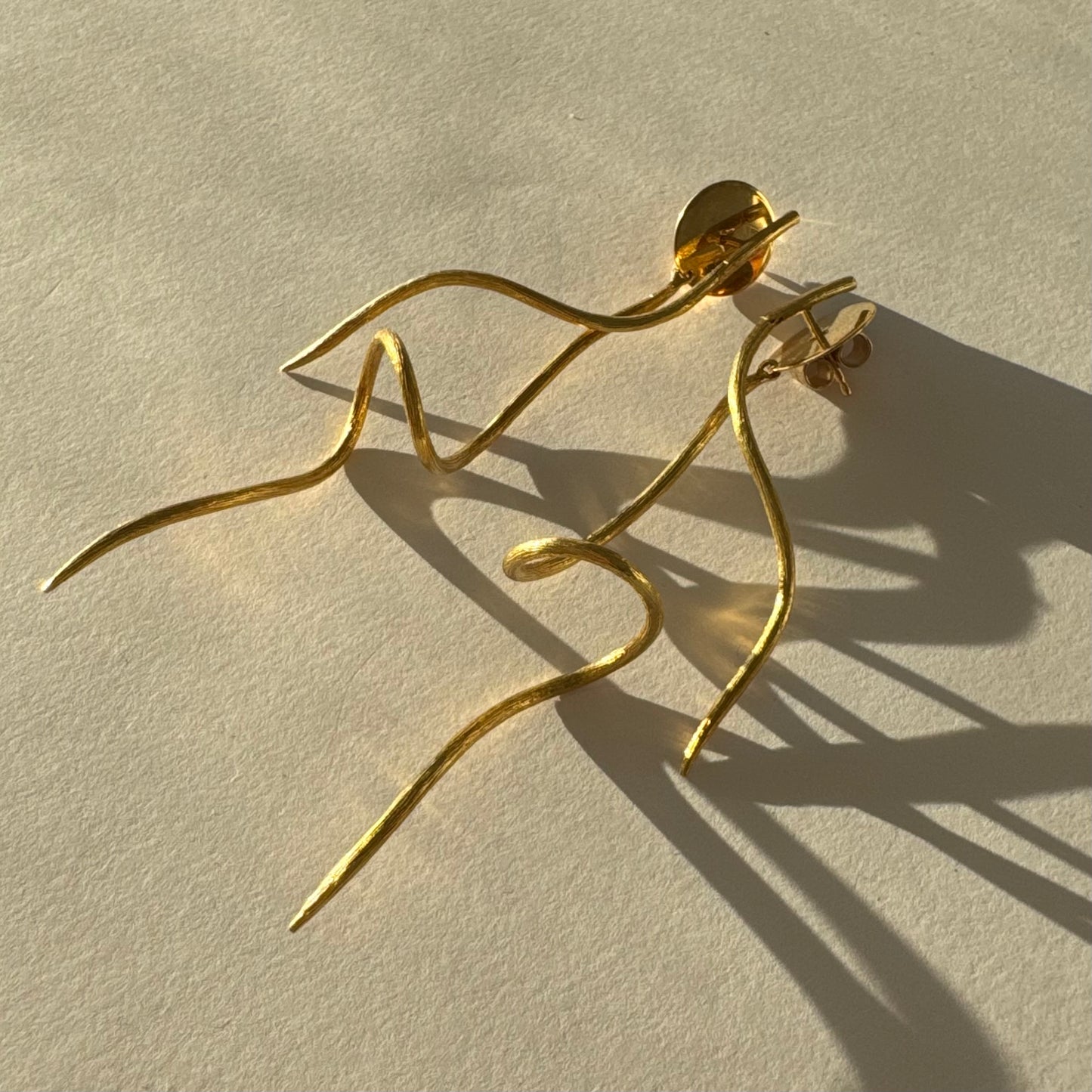 עגילי זהב צהוב 18 קראט מבית ה.שטרן, בעיצוב פיסולי וייחודי עם קווים זורמים ודינמיים.