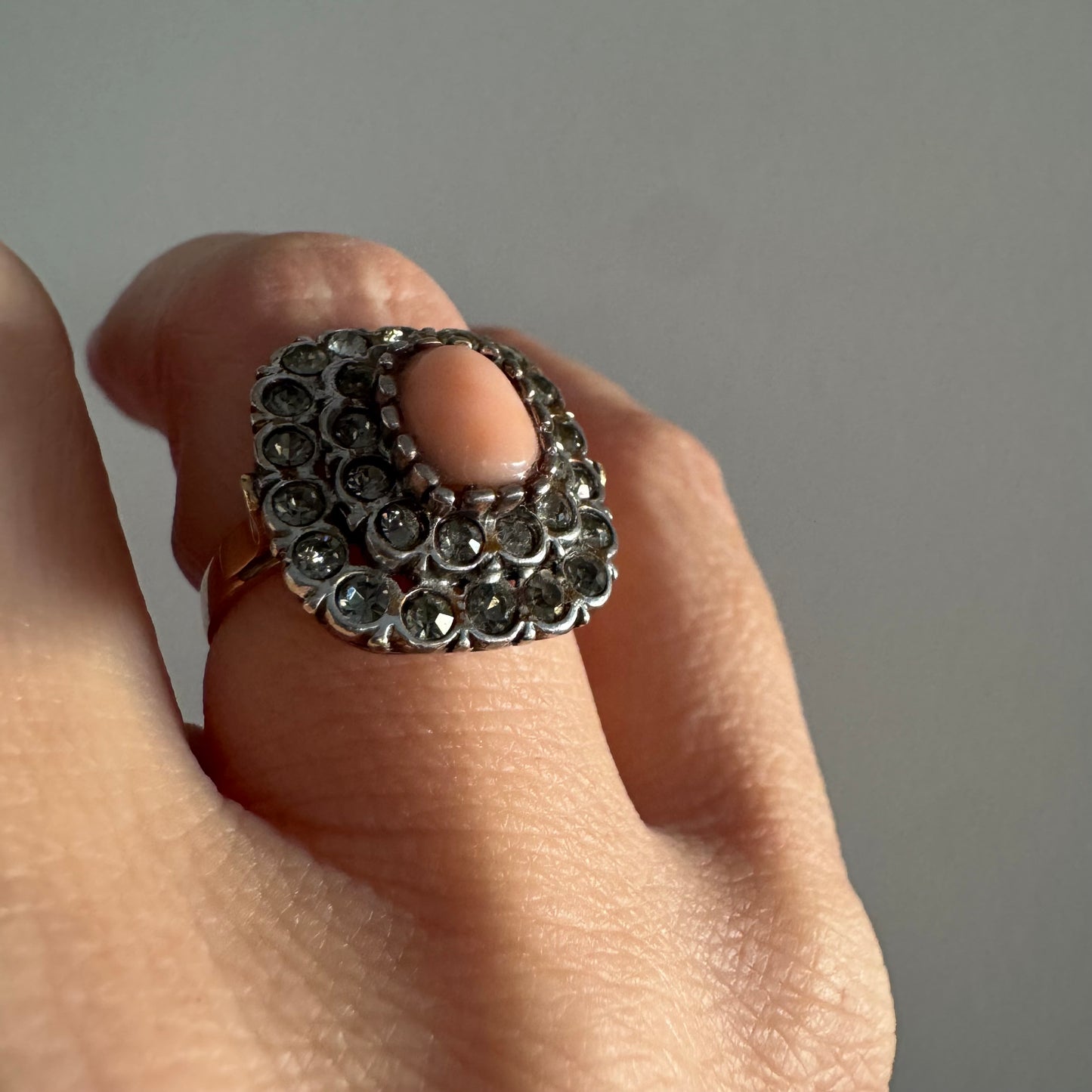 טבעת וינטג׳ עם חלק תחתון מזהב 14 קראט וחלק עליון עשוי כסף משובצת אבן קורל טבעית במרכז ומסביבה אבנים בהירות שאינן יהלומים.