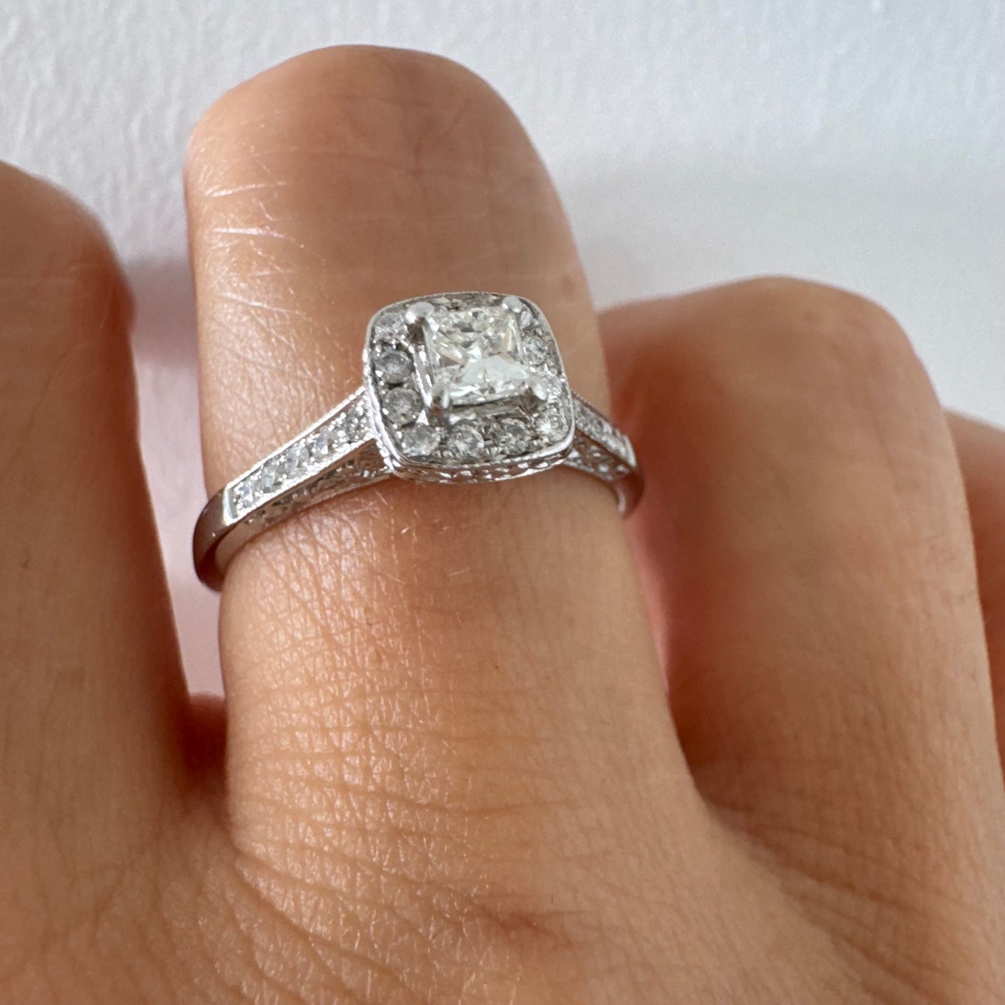 טבעת זהב לבן 14 קראט משובצת יהלום מרכזי בחיתוך פרינסס, מוקף הילת יהלומים קטנים וזרוע משובצת פאווה