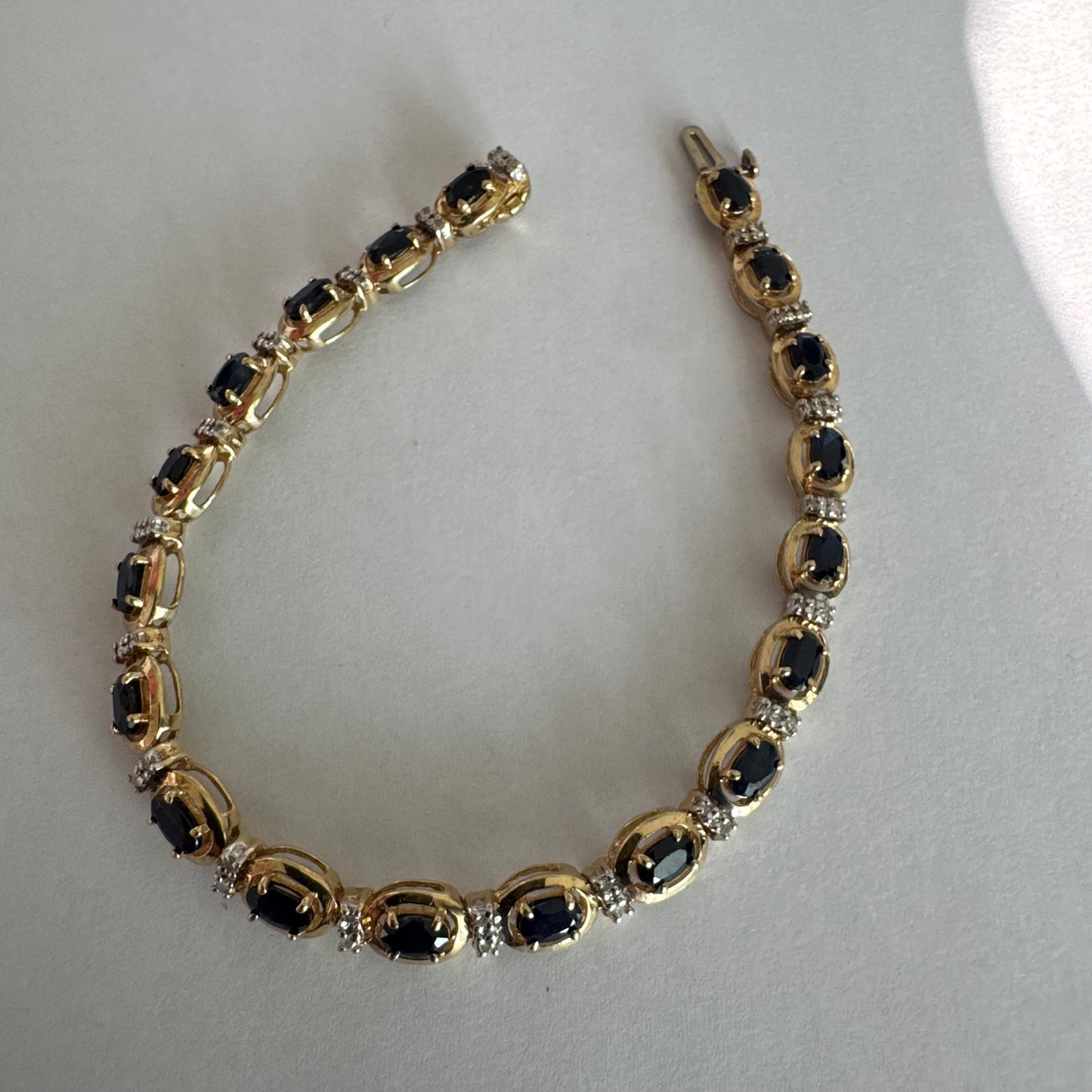 צמיד זהב צהוב 10 קראט בעיצוב קלאסי ועשיר, משובץ אבני ספיר אובליות בגוון כחול עמוק וביניהן שיבוצי יהלומים לבנים עדינים.