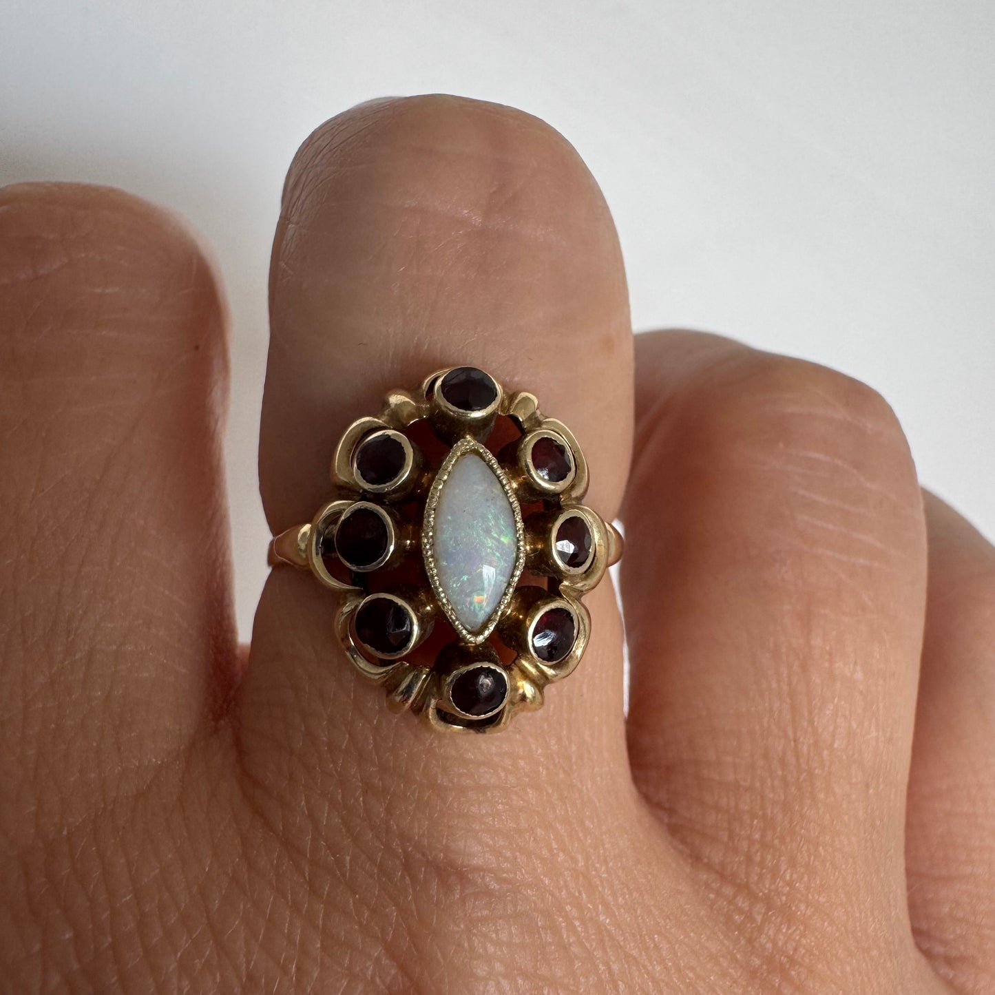 14K gold ring set with a luminous marquise-cut Opal at the center, surrounded by deep red Garnet cabochons