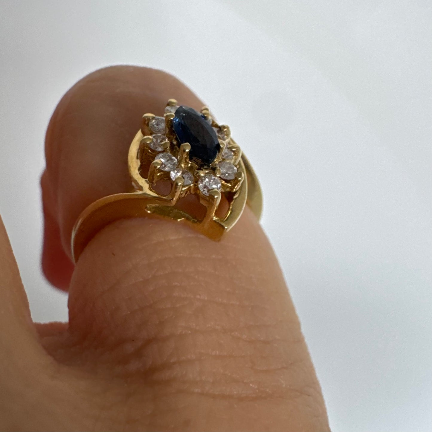 טבעת זהב צהוב 18 קראט משובצת ספיר כחול מרכזי בחיתוך מרקיזה, מוקף הילה של יהלומים המעניקים ניצוץ עדין ומדגישים את צבע האבן העמוק.