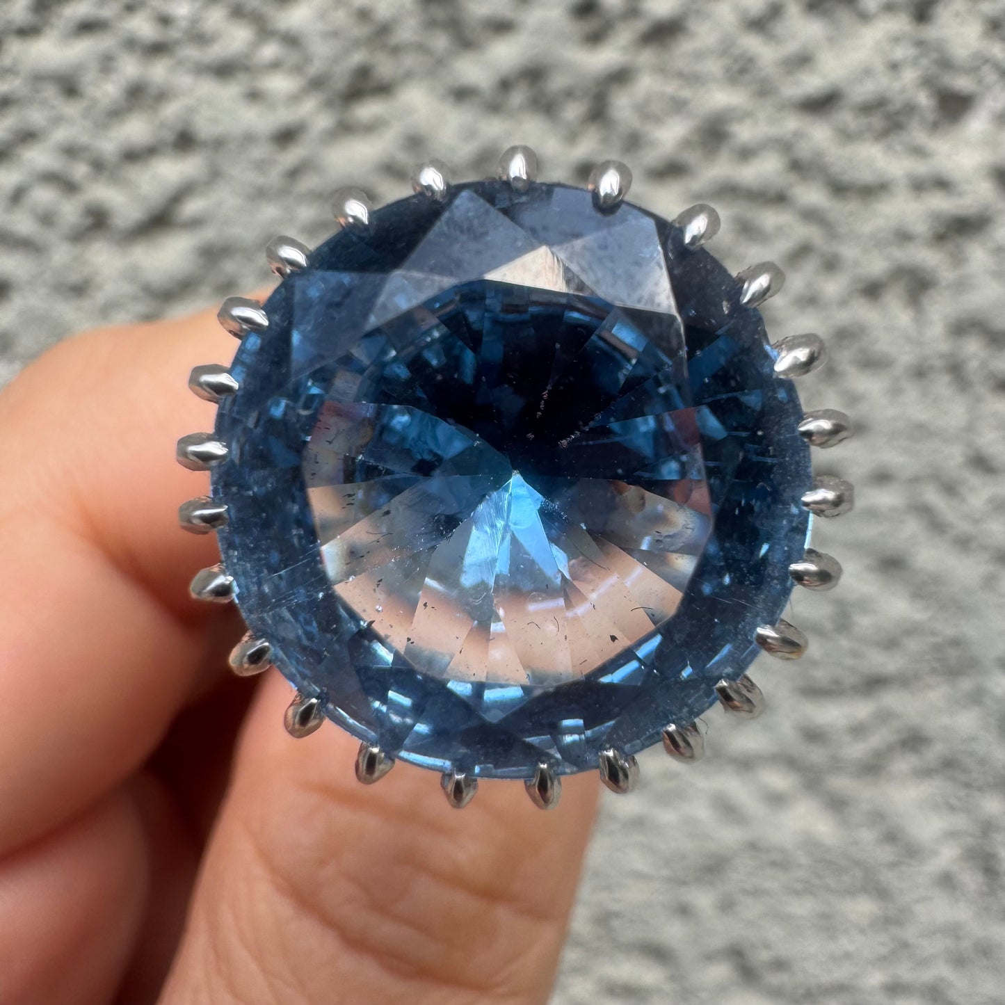 טבעת זהב לבן 14 קראט משובצת אבן טופז בצבע כחול, בולטת, בחיתוך עגול, משובצת במסגרת שיניים גבוהה ליצירת מראה מרשים ותופס עין