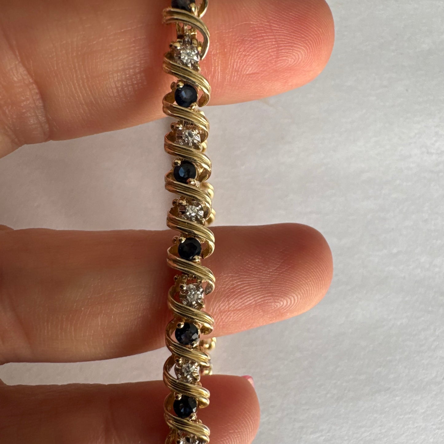 צמיד זהב צהוב 14 קראט משובץ אבני ספיר כחולות ויהלומים, המשובצים בעיצוב זורם עם קווים מעוגלים העוטפים כל אבן.