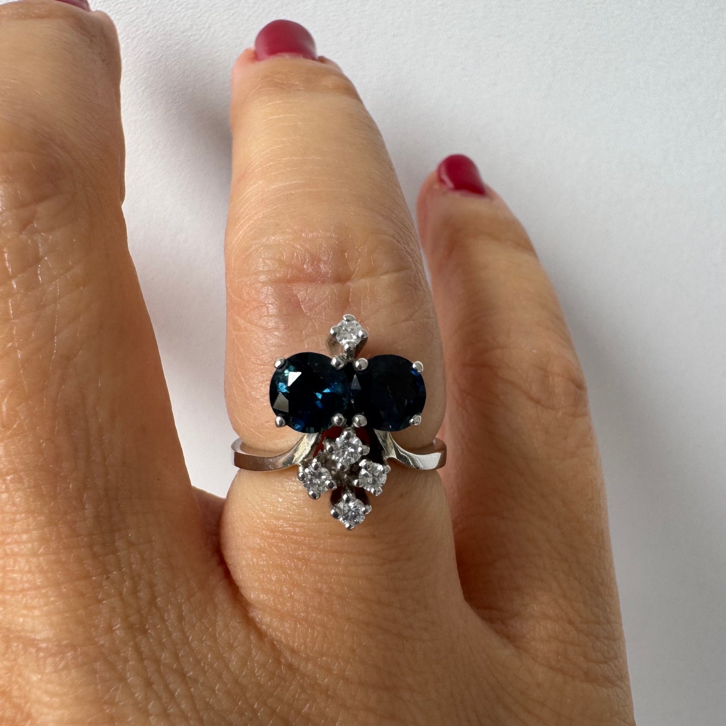 14K gold ring set with two deep blue oval Sapphires accented by clusters of brilliant white Diamonds.