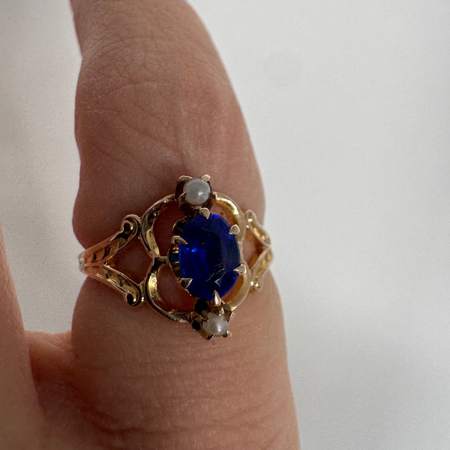 טבעת זהב צהוב 10 קראט משובצת אבן ספיר אובלית בגוון כחול עמוק ועשיר, ולצידה פנינים קטנות עדינות מעל ומתחת לאבן.