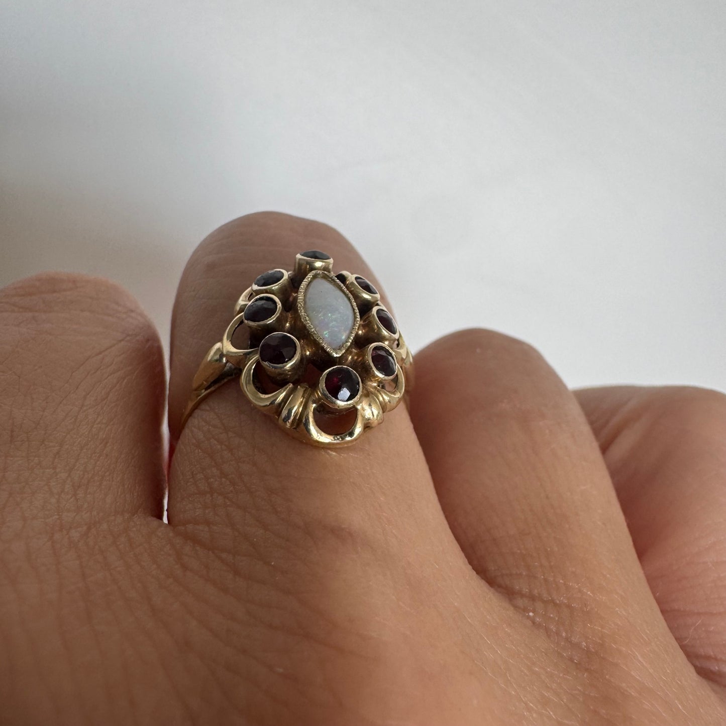 14K gold ring set with a luminous marquise-cut Opal at the center, surrounded by deep red Garnet cabochons