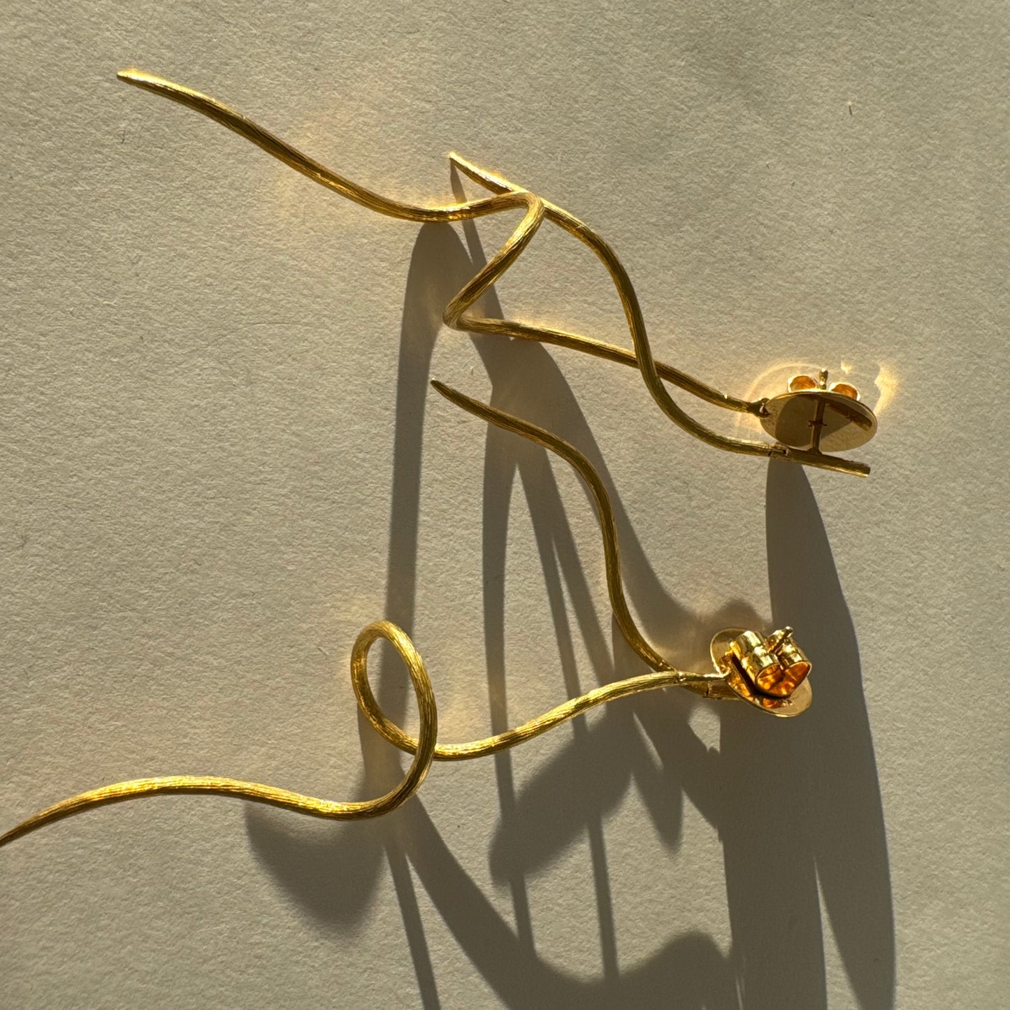 עגילי זהב צהוב 18 קראט מבית ה.שטרן, בעיצוב פיסולי וייחודי עם קווים זורמים ודינמיים.