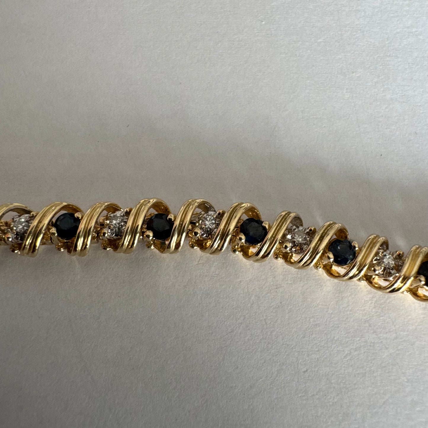 צמיד זהב צהוב 14 קראט משובץ אבני ספיר כחולות ויהלומים, המשובצים בעיצוב זורם עם קווים מעוגלים העוטפים כל אבן.