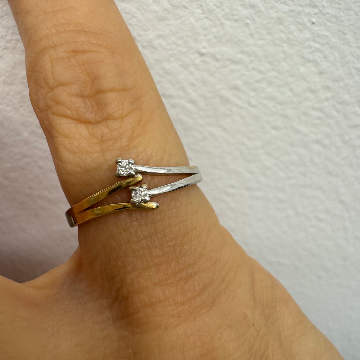 טבעת זהב 14 קראט, עם זרועות מצטלבות בזהב צהוב וזהב לבן, שכל אחת מהן משובצת יהלום קטן ונוצץ.