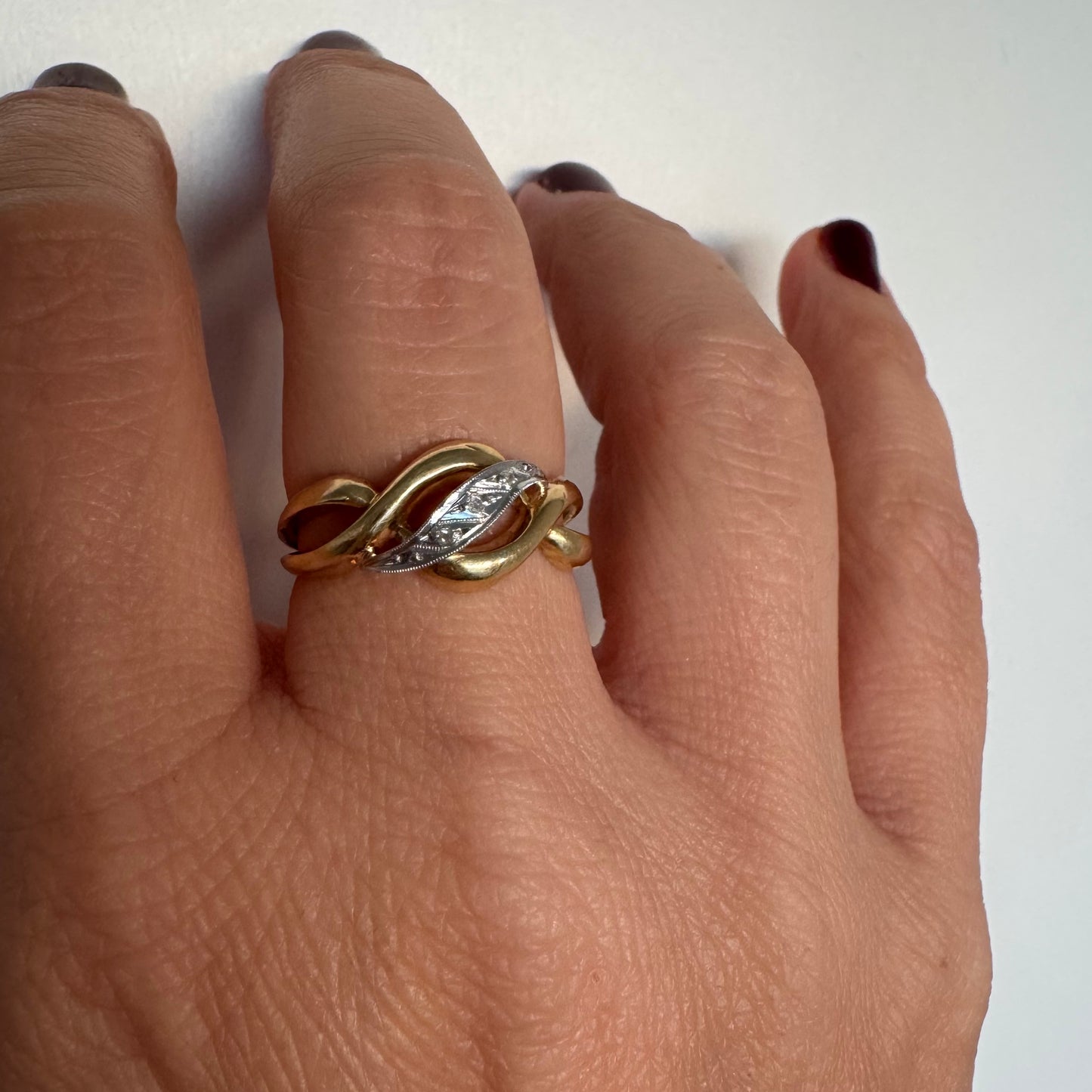 טבעת זהב צהוב 18 קראט בעיצוב קשר קלאסי, בשילוב אלמנט מרכזי מזהב לבן משובץ יהלומים עדינים.