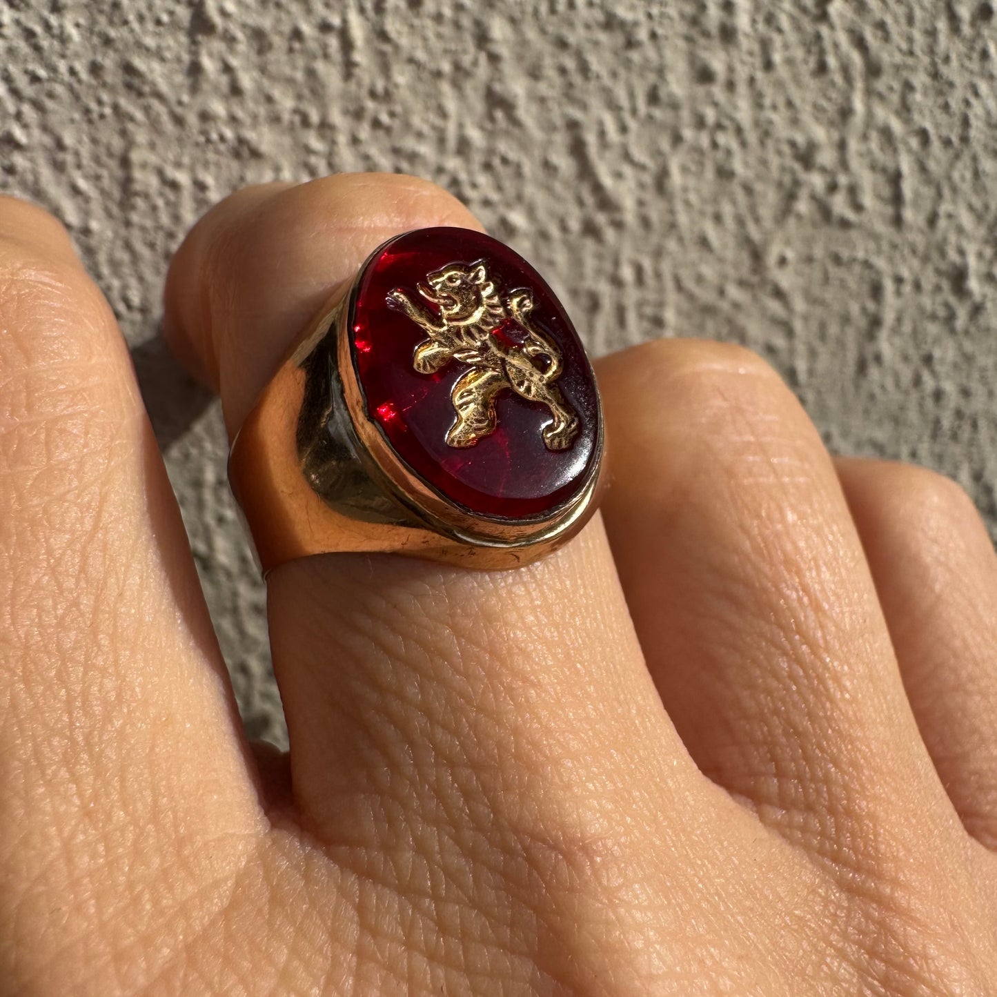 טבעת חותם זהב צהוב 14 קראט משובצת אבן אדומה חלקה ודמות אריה מוזהבת בעיצוב עתיק.