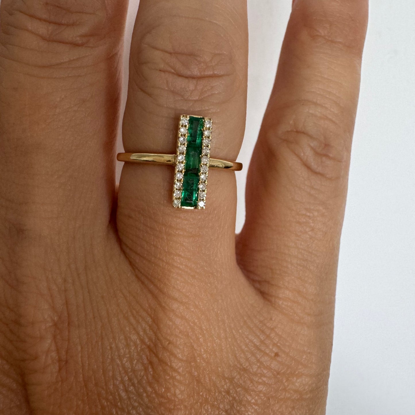 טבעת זהב 14 קראט משובצת אבני אמרלד בחיתוך באגט, מוקפות בשתי שורות של יהלומים נוצצים .